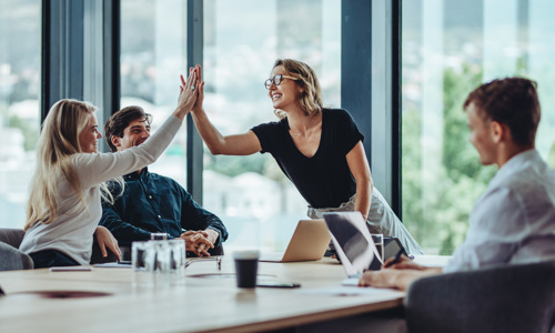 Two employees high-fiving each other around a table in a professional environment