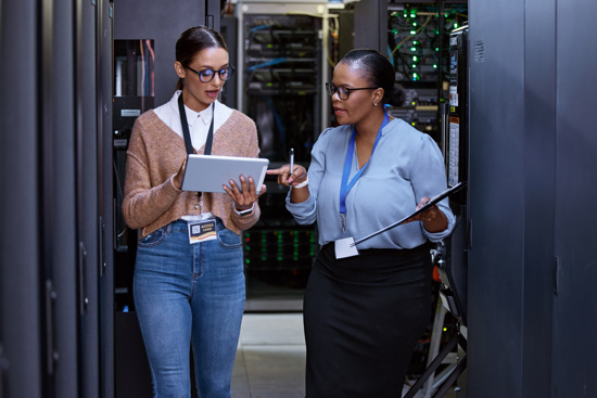 Two employees discussing information on a tablet in a server room