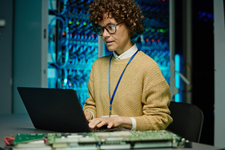 A person sitting at a laptop in an environment with a large server wall in the background