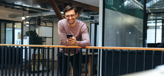 A man looking at his phone while leaning on a balcony inside a building