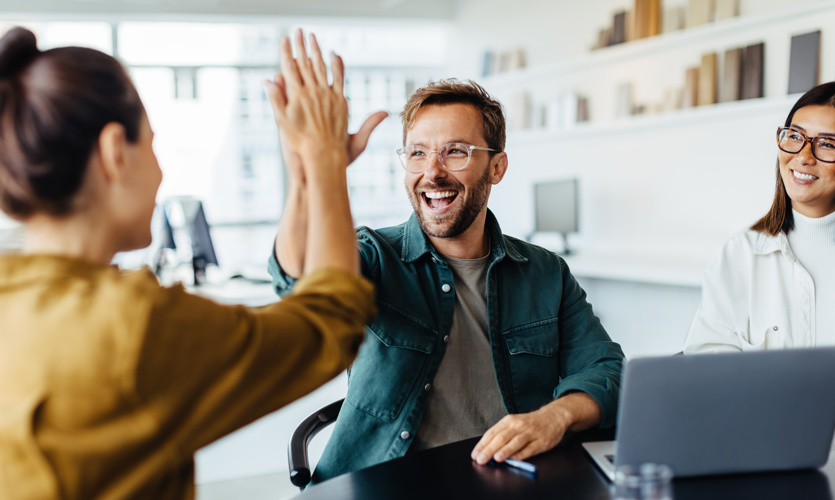 A man and a woman high fiving each other while sitting at a desk