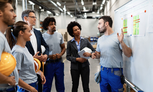 One employee presenting information from a whiteboard to a group of fellow employees 